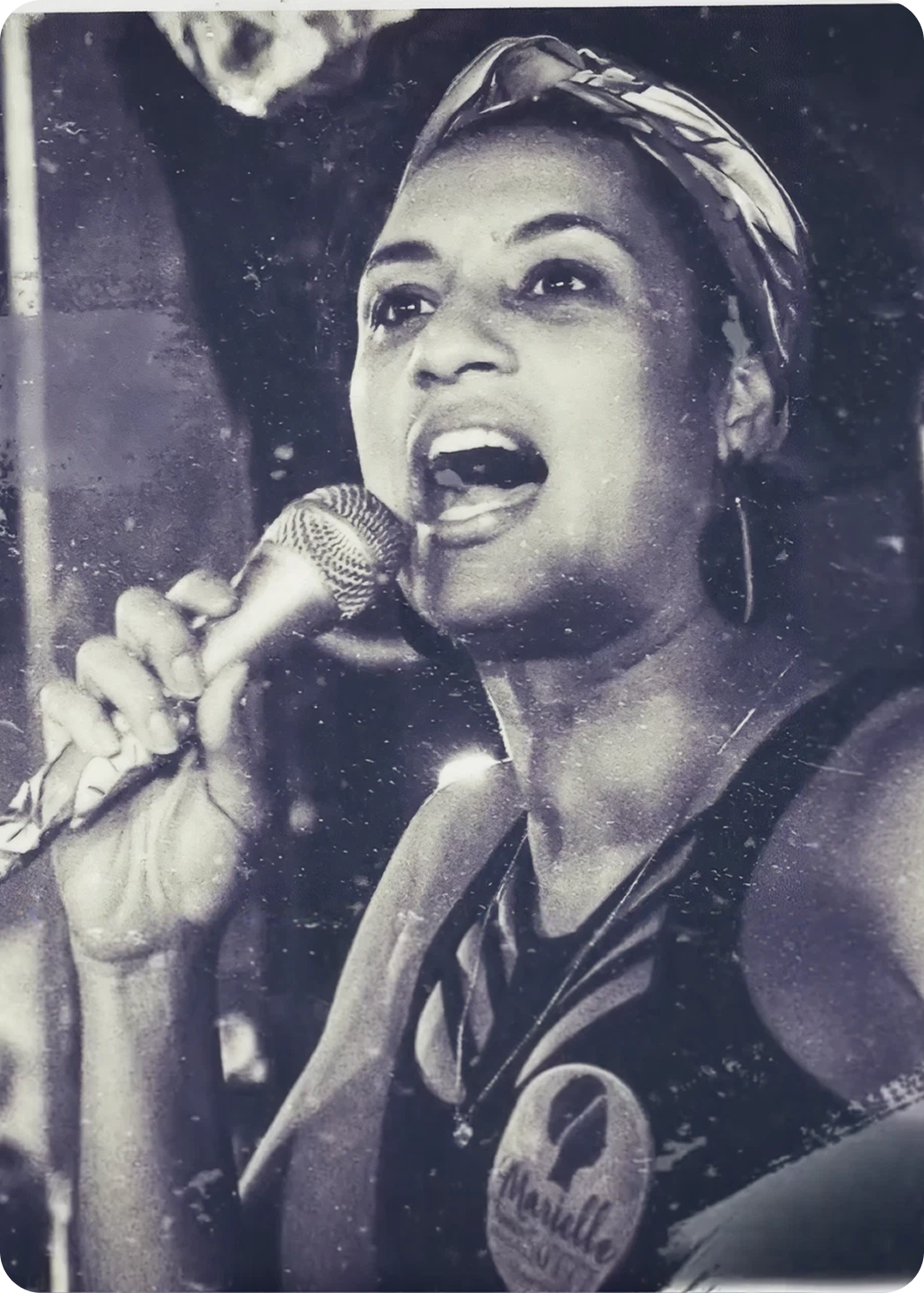 Foto en blanco y negro de una mujer cantando al micrófono, de la pieza de aniversario de Amnistía Internacional Brasil.